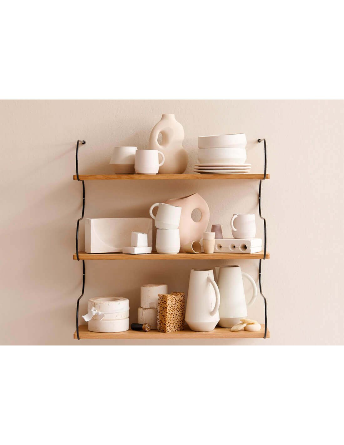 Étagère murale en bois et métal avec vaisselle et objets décoratifs blancs et neutres, stacks de plats et carafes sur trois niveaux.