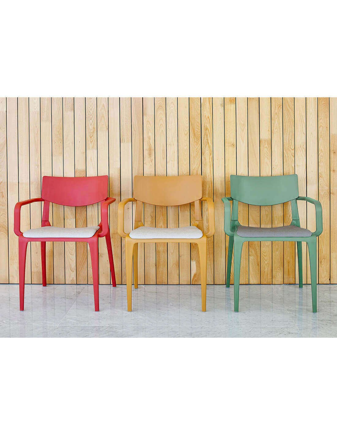 Trois chaises design colorées alignées contre un mur en lamelles de bois, assises blanches et matériaux plastiques à l’allure moderne.