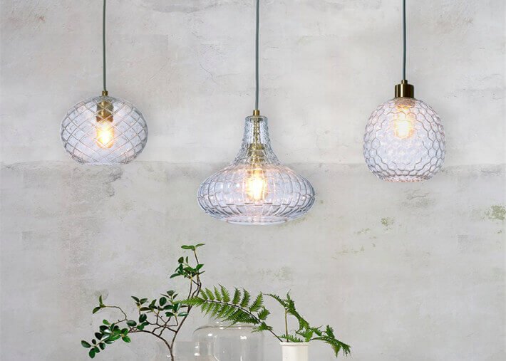 Trois suspensions lumineuses en verre cristal, éclairant une table avec plantes; contraste entre lustre et suspension expliqué.